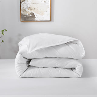 Folded white comforter on a light gray surface with a neutral wall and framed abstract art in the background.