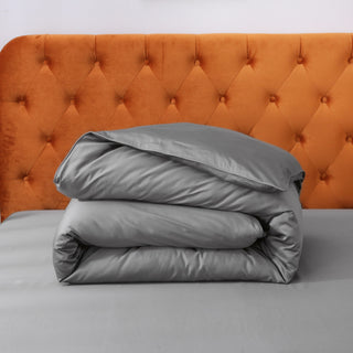 Gray comforter on a bed with an orange tufted headboard