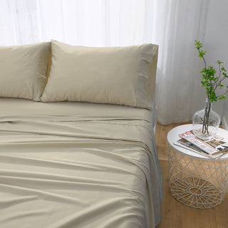 Beige bed sheets and pillows on a bed with a side table and a plant in the background