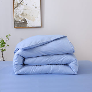 Folded light blue comforter on a bed with a neutral wall and plant in the background
