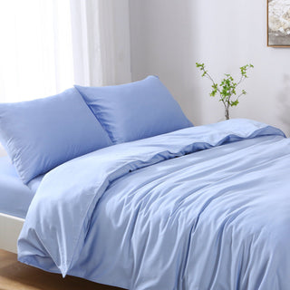 Blue bedding set on a bed with white curtains and a plant in the background