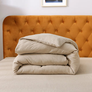 Folded beige comforter on a bed with an orange tufted headboard.