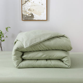Folded light green comforter on a bed with a minimal background