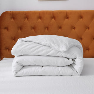 Folded white comforter on a bed with an orange tufted headboard.