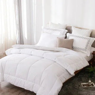 White comforter and pillows on a bed with light curtains in the background