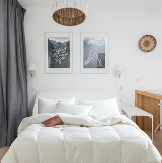 Neatly made bed in a bedroom with white walls, a wooden side table, and framed artwork.