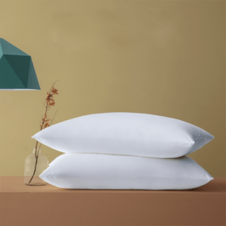 Two white pillows are stacked on a brown surface with a beige wall in the background.