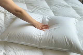A hand pressing down a fluffy down pillow