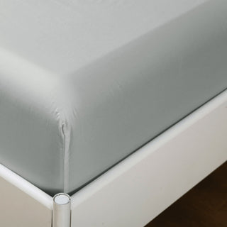 Gray fitted sheet on a bed corner with a white bed frame.