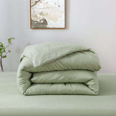 Folded light green comforter on a bed with a minimal background