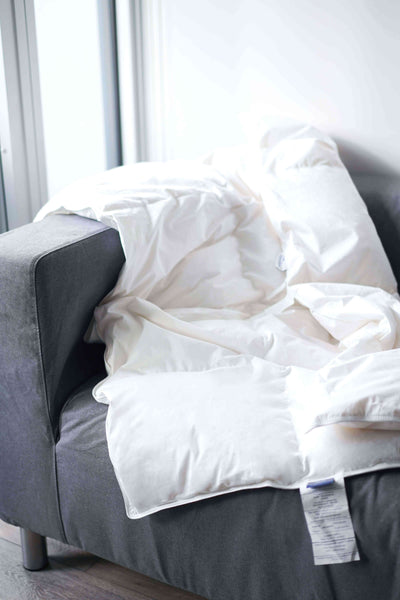 White comforter on a gray sofa with a blurred window background