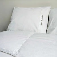 White bedding set with personalized pillowcases on a bed.